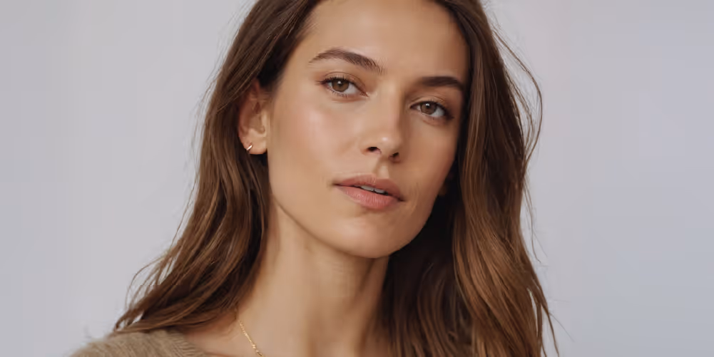 A woman with long, wavy brown hair and natural makeup is looking directly at the camera with a subtle expression.