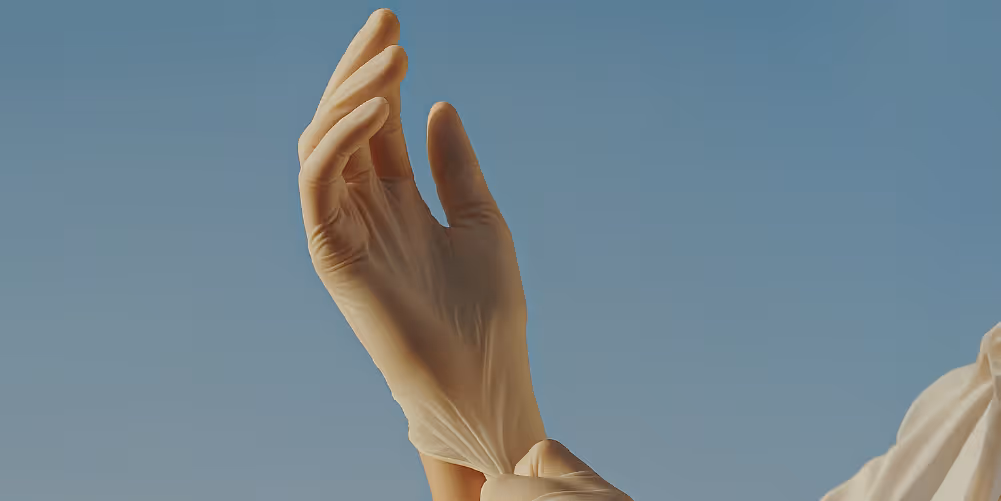 A gloved hand pulling on a medical glove, with fingers slightly bent.
