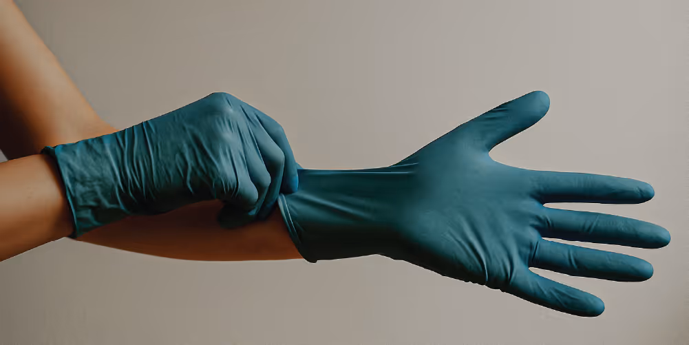 A person wearing teal examination gloves, pulling the gloves onto their hands.