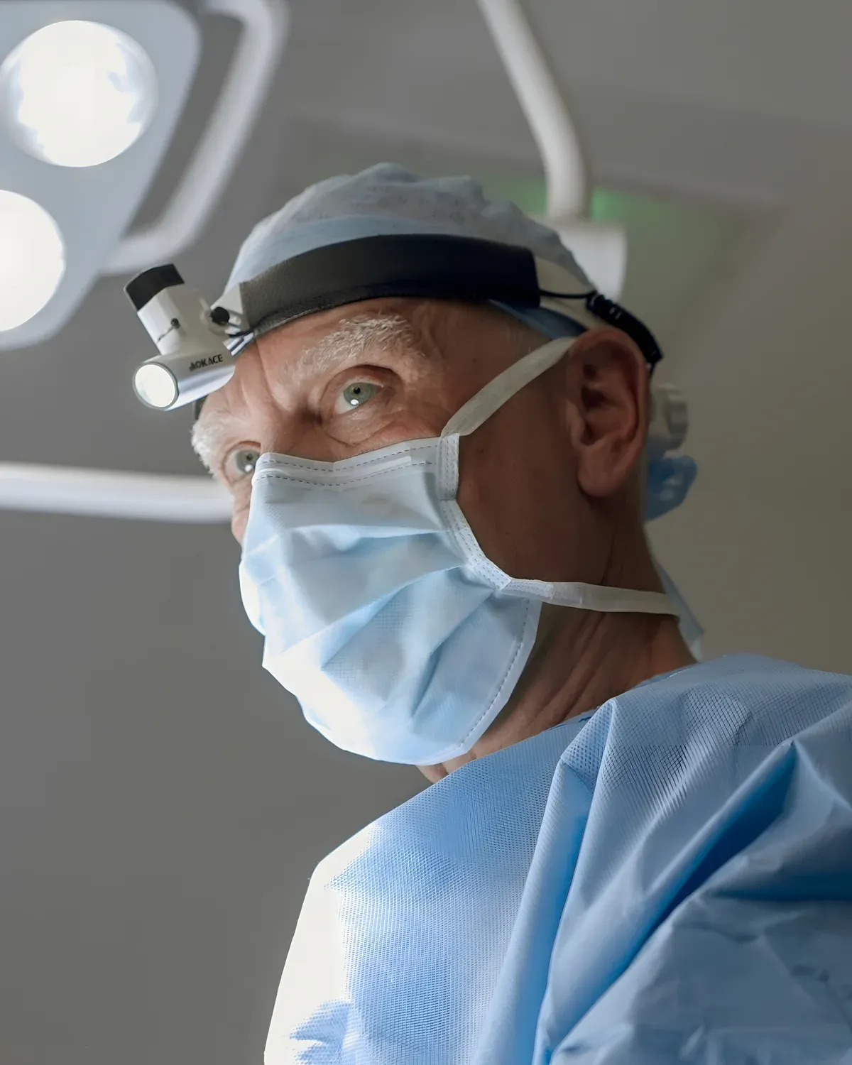 Surgeon in mask, cap and headlight under operating theatre lights